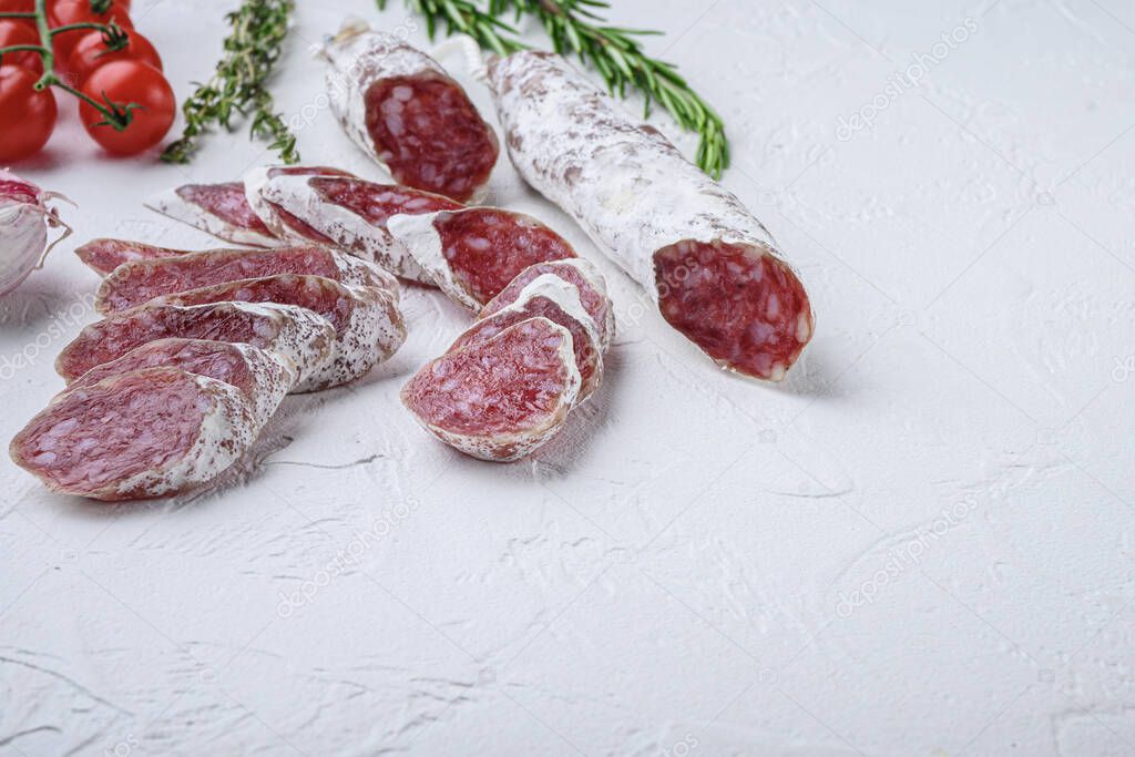 Dry cured fuet salami sausage slices with herbs on white textured background with space for text.