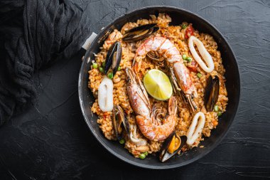 Paella geleneksel İspanyol yemeği kızartma tavasında servis edilir, siyah desenli yüzey, üst manzara, yemek fotoğrafı..