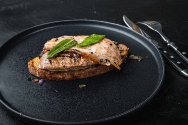 Ekmeğin üstünde domuz pastırması ve soğan. Siyah yüzeyde tabakta pişmiş yemek..