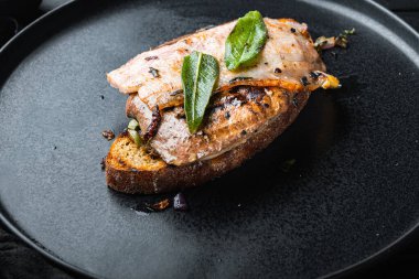 Ekmeğin üstünde domuz pastırması ve soğan. Siyah yüzeyde tabakta pişmiş yemek..