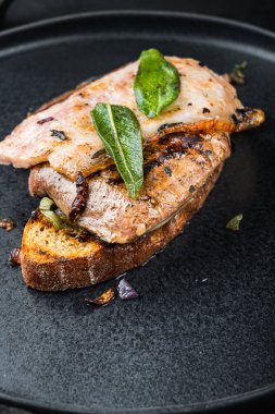 Ekmeğin üstünde domuz pastırması ve soğan. Siyah yüzeyde tabakta pişmiş yemek..