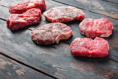 Çeşitli organik çiğ biftek biftekleri. Kalça, yuvarlama ve üst bıçak. Eski, kırsal, siyah ahşap arka planda kesilmiş.