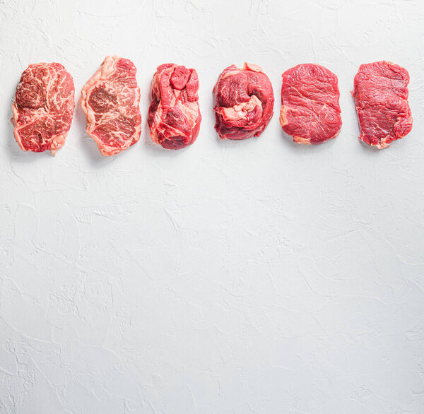 Rraw beef steaks set top blade, rump, chuck eye roll over white concrete background, top view space for text