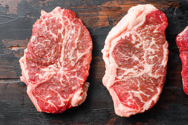 Set of aw beef top blade steaks on old wooden dark planks top view