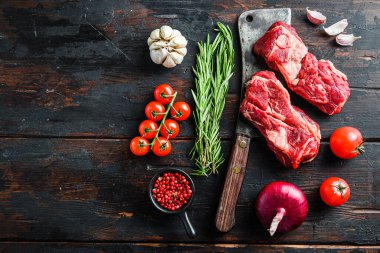 Eski kasap satırı üzerine organik çiğ Chuck bifteği, kırmızı biberiye, sarımsaklı biber ve domatesler eski, siyah ahşap masa üzerinde. Metin için boşluk olan üst görünüm