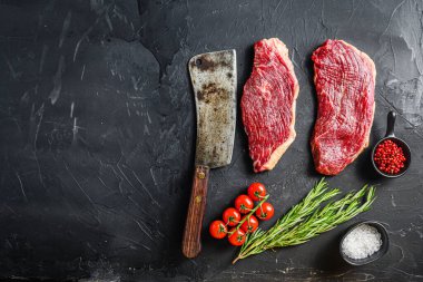 Biberiyeli çiğ biftek, biberiye, biber ve siyah desenli arka planda eski kasap satırı yakınında tuz, metin için üst görüş alanı