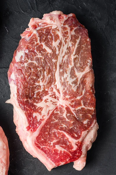 Organic top blade beef  steaks, top view on black textured table.