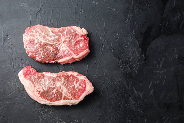 Raw top blade steak cuts, top view on black textured background with space for text