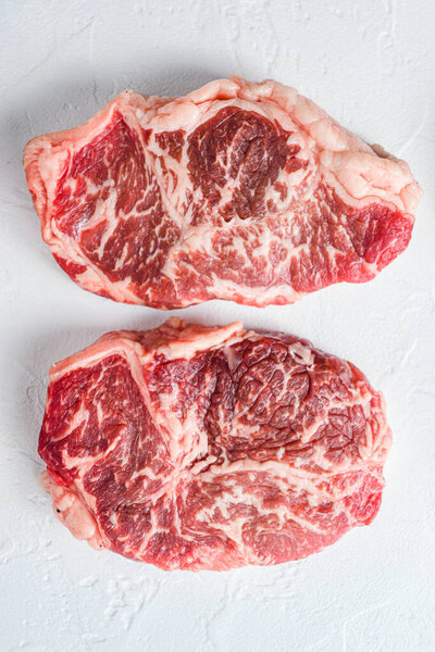 Raw top blade steak. Organic beef. White textured background. Top view
