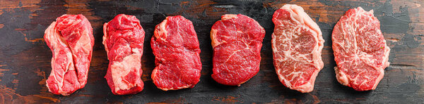 A set of different types of raw beef steaks:top blade, rump, chuck eye roll over old wooden background top view banner size