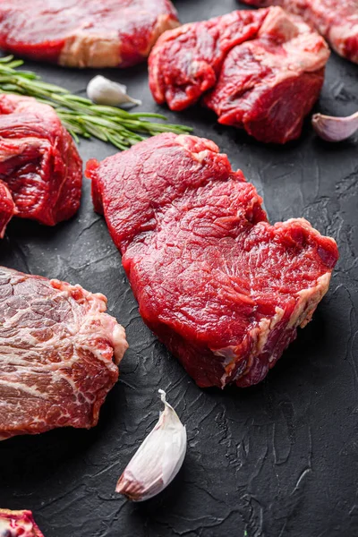 Rump beef steak cuts, with herbs, seasoning  on black table, side view