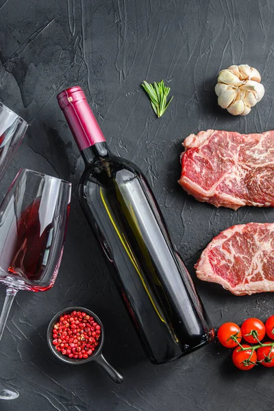 Bottle of red wine with glasses near beef steak raw cuts, top view space for text