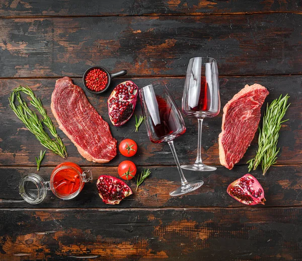 Picanha Center-Cut Steak with glasses of red wine, herbs and pomegranate top view over old dark wooden table. Big size