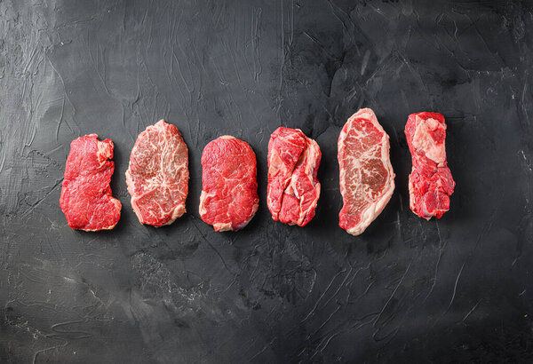 Variety of raw alternative steaks picanha, ramp and chuck eye roll and top blade over black background top view. Big size. Space for text