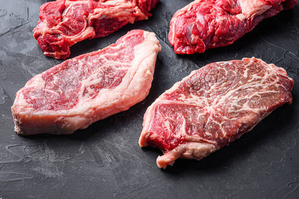 Two raw organic top blade beef  steaks, side view on black textured table