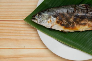 Muz yaprağına yerleştirilmiş ızgara balığı kopyalama alanı olan beyaz bir tabakta kapat..