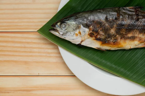 Muz yaprağına yerleştirilmiş ızgara balığı kopyalama alanı olan beyaz bir tabakta kapat..