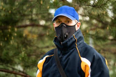 Solunum maskesi ve açık havada şapka takan bir adam..