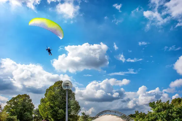 公園の上の青い曇りの空に緑の木々の上にパラシュートを使用して滑空 — ストック写真