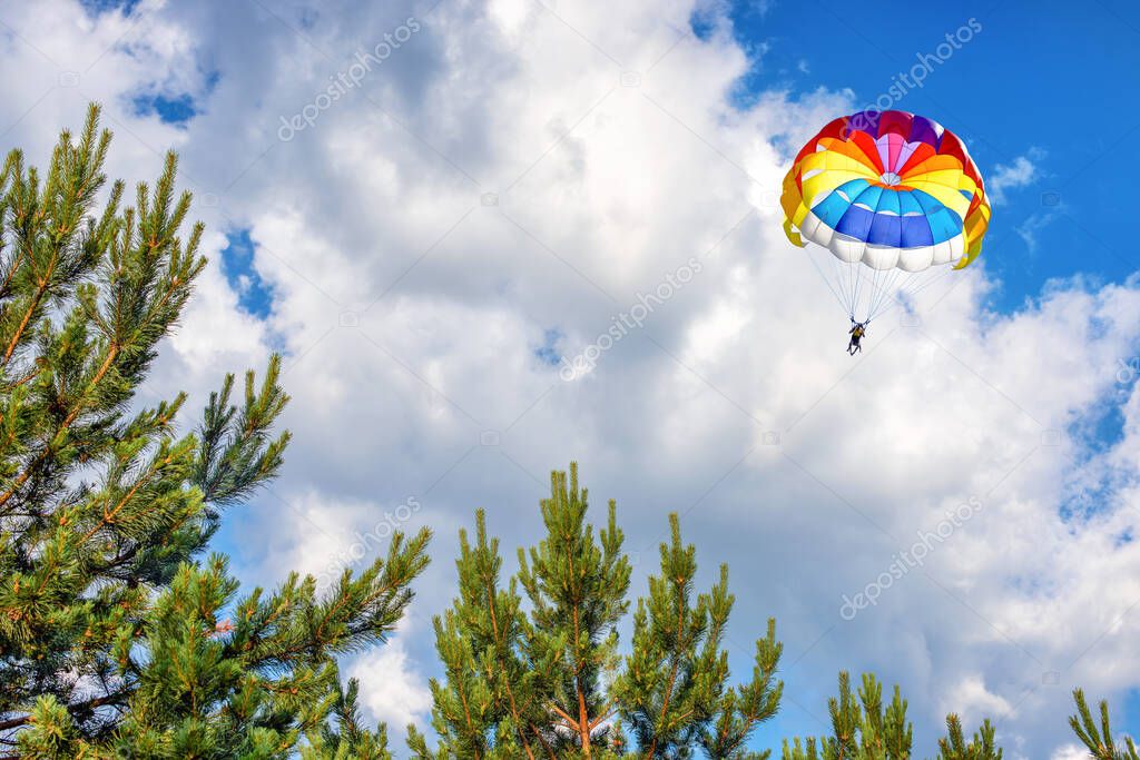 Paragliding parachuting sport in the blue cloudy sky over the forest.