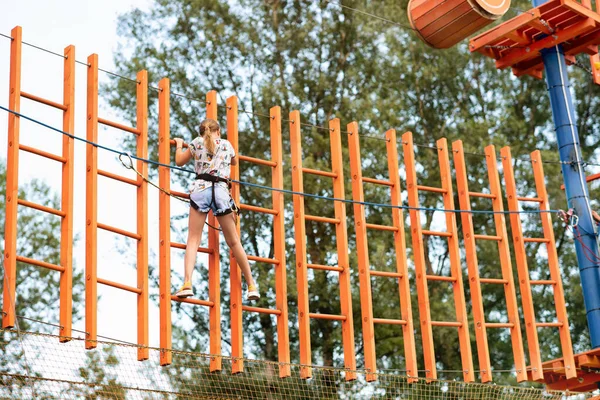 ロシアのアバカン 2020年7月19日 女の子は夏に極端なスポーツパークでサイドロープを保持ハンギングブリッジを通過しようとします — ストック写真