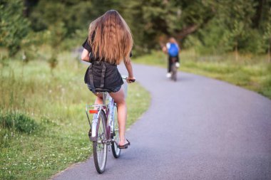 Yazın güneşli bir sabahta parkta bisiklet süren bir kız..