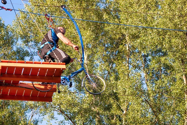 ロシアのアバカン 2020年7月19日 男は夏に極端なスポーツパークで自転車にサイドロープを保持ハンギングブリッジを通過しようとします — ストック写真