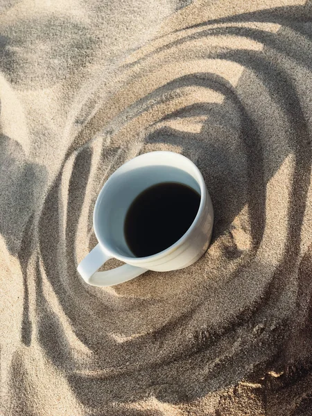 White cup of coffee on the sand on the beach