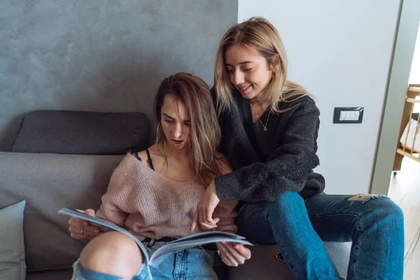 Två unga flickor i en soffa titta på tidningen — Stockfoto