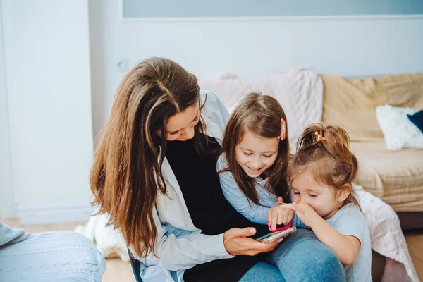 Maminka a dvě dcery hledají smartphone — Stock fotografie