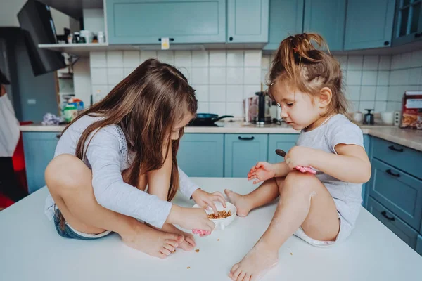 Two little girls in the kitchen sitting on the table. — Stock Photo, Image