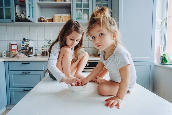 Zwei kleine Mädchen in der Küche sitzen auf dem Tisch. — Stockfoto