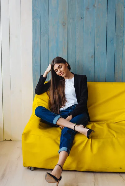Jeune femme assise sur un canapé jaune — Photo