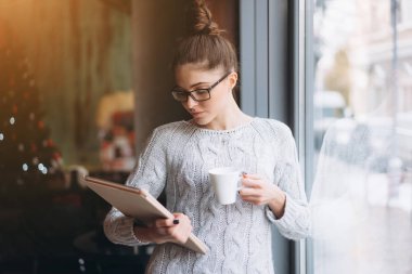 Tablet vasıl seyir ve büyük pencereli kafede gülümseyen genç kız.