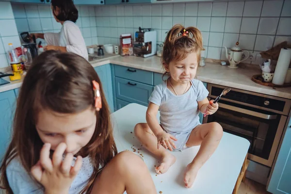 Two little girls in the kitchen sitting on the table. — Stock Photo, Image
