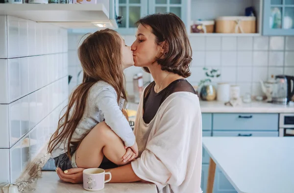 Мама целует свою маленькую дочь на кухне — стоковое фото