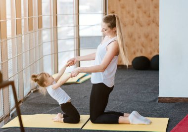 Anne ve kızı birlikte farklı egzersizler yapıyorlar.