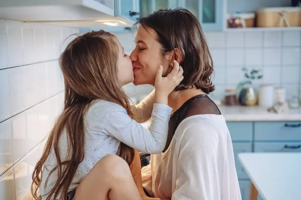 Mãe beija sua filhinha na cozinha — Fotografia de Stock