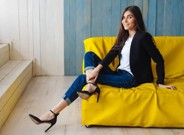 Jeune femme assise sur un canapé jaune — Photo