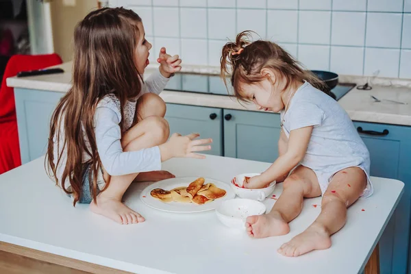 Duas meninas na cozinha sentadas na mesa. — Fotografia de Stock