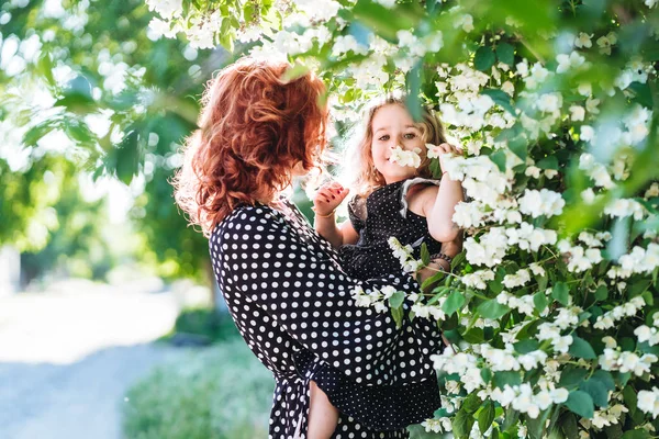 Young woman stands near jasmine with a small daughter — Stock Photo, Image