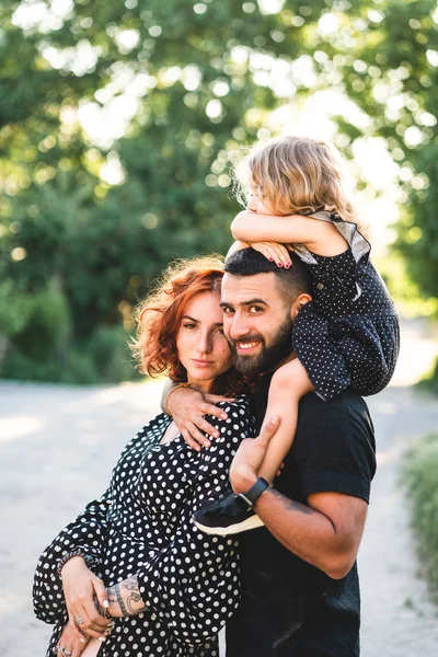 Lyckliga föräldrar med en liten dotter som sitter på axlarna — Stockfoto