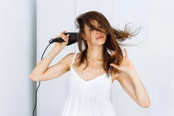 Mulher de roupão de banho secando o cabelo com secador sobre fundo branco — Fotografia de Stock