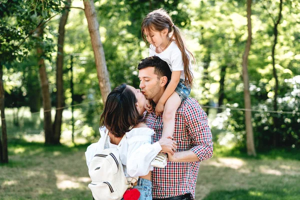 Glückliche junge Eltern küssen sich im Park. — Stockfoto