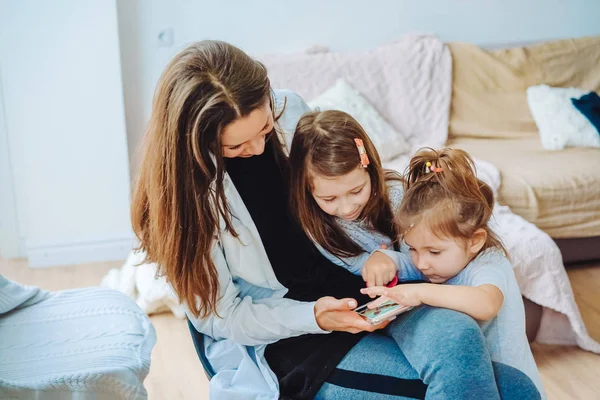 Mutter und zwei Töchter schauen aufs Smartphone — Stockfoto