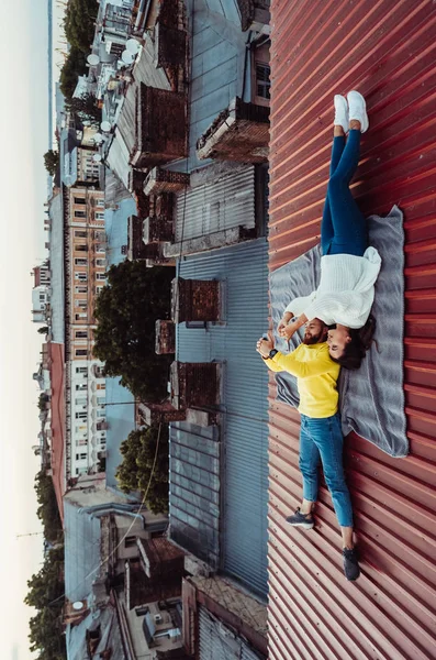 Een knappe jongen en een jong meisje liggen op het dak en houden de slimmeriken vast. — Stockfoto