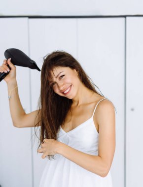 Beyaz arka plan üzerinde saç kurutma makinesi ile kurutma bornoz kadında