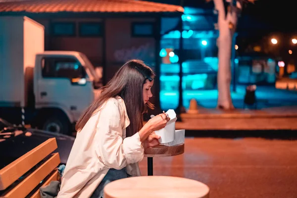 A menina está comendo fast food, na rua da cidade da noite — Fotografia de Stock