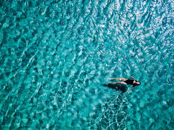 Menina em um maiô preto nada no mar . — Fotografia de Stock