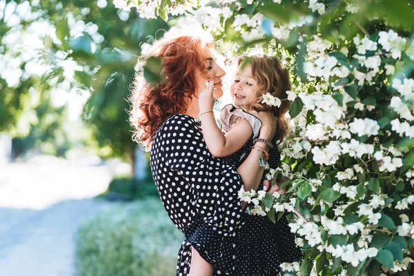 Mujer joven se para cerca de jazmín con una hija pequeña —  Fotos de Stock